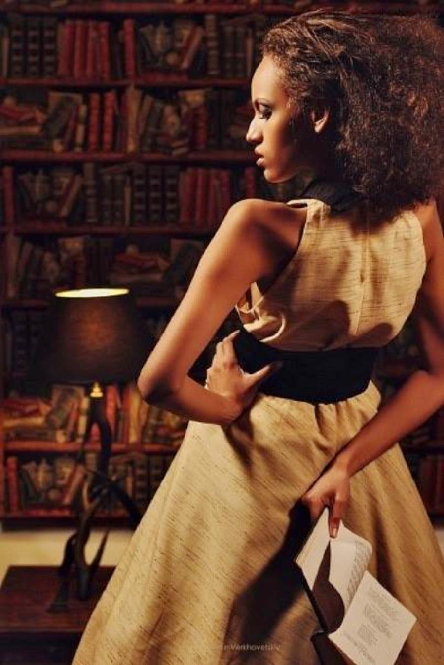 Дівчина в елегантному вбранні 50-х років з книгою в руках на фоні бібліотеки